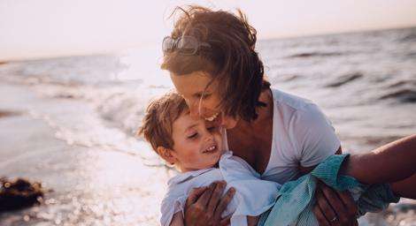 Woman holding young boy on a sunny beach next to the sea