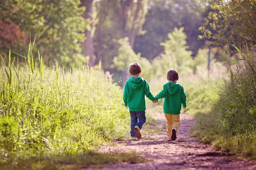 Two boys in green hoodies holding hands and walking down a forest path